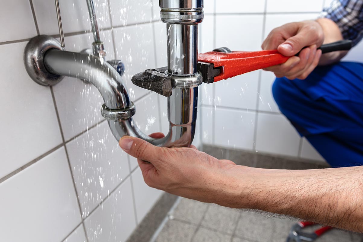 Plombier réparant le siphon d'un lavabo qui fuit de l'eau dans une salle de bain